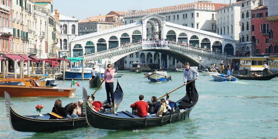 "Gondoliers transporting tourists on the scenic Grand Canal in Venice, Italy with the iconic Rialto Bridge in the background. The picture was taken next to Riva del Vin in the charming Sestriere Dorsoduro neighborhood. Experience the charm and romance of Venice's waterways with this quintessential image."